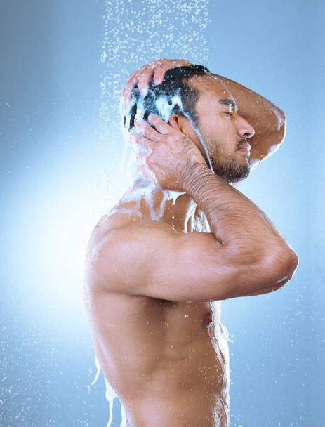 Estudio de un joven guapo lavándose el pelo en una ducha sobre un fondo gris. - Foto, Imagen