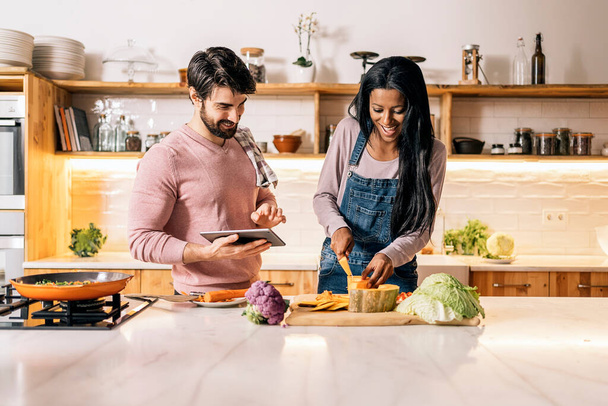 Cute couple preparing lunch together in the kitchen at home and using tablet. - Zdjęcie, obraz