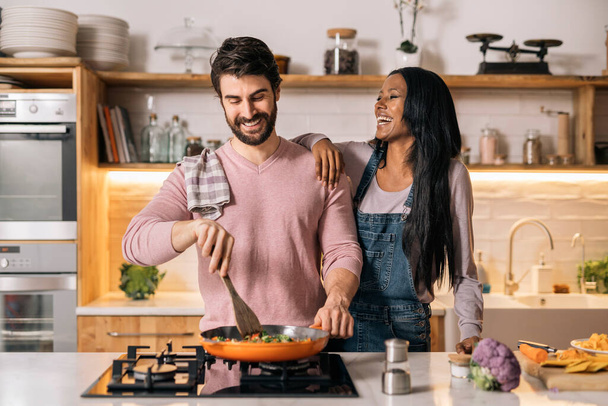 Cute couple smiling and preparing lunch together in the kitchen at home. - Foto, Bild