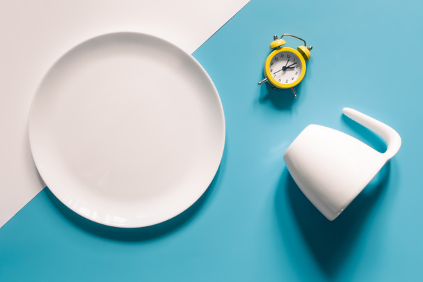 Empty plate, cup and alarm clock on a blue background, intermittent fasting, Ketogenic dieting, weight loss, meal plan, and healthy food concept. - Zdjęcie, obraz