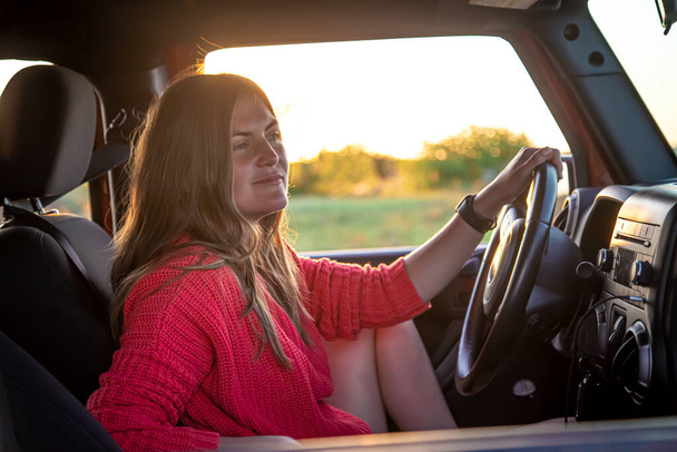 A young woman driving a red SUV in the countryside at sunset. - Φωτογραφία, εικόνα
