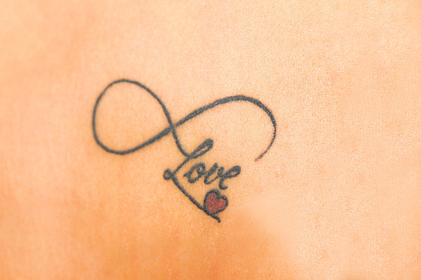 photo of abstract tattoo on skin that says love with smal red he - Photo, Image