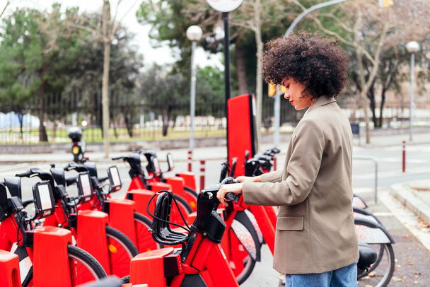 young woman taking an electric bike from a bike rental station, active lifestyle and sustainable mobility concept - Foto, immagini