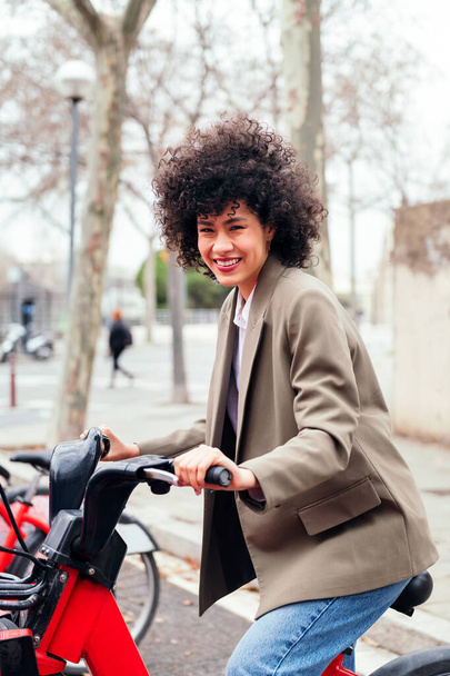 smiling young woman rides an electric bike from a rental station, active lifestyle and sustainable mobility concept - Фото, изображение