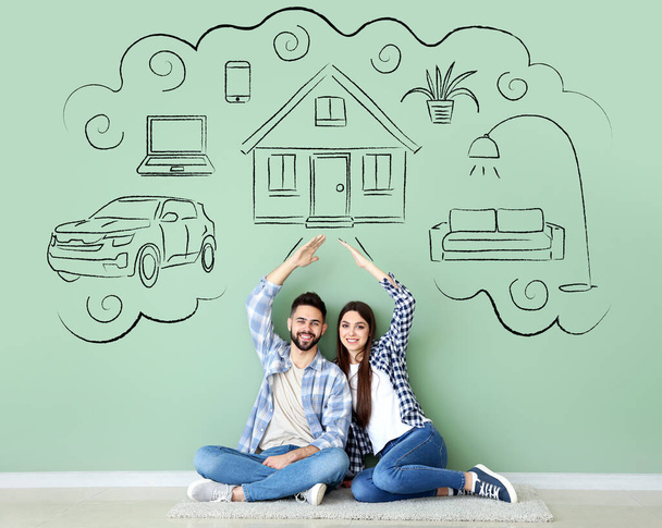 Jovem casal sonhando com sua nova casa e carro perto de parede verde no quarto - Foto, Imagem