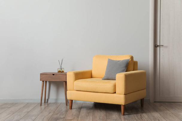 Comfortable armchair with table and air freshener near light wall in room - Foto, afbeelding