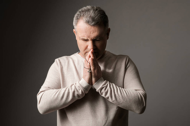 Praying mature man with cross on dark background - Foto, afbeelding