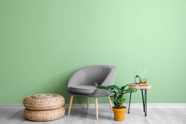 Mukava nojatuoli pöytä ja huonekasvi lähellä vihreää seinää huoneessa - Valokuva, kuva