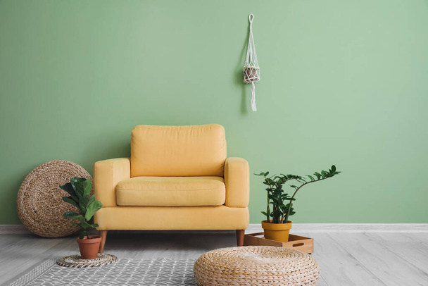 Удобное кресло с комнатными растениями рядом с зеленой стеной в номере - Фото, изображение