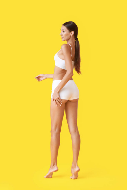 Young tanned woman in underwear on yellow background - Zdjęcie, obraz