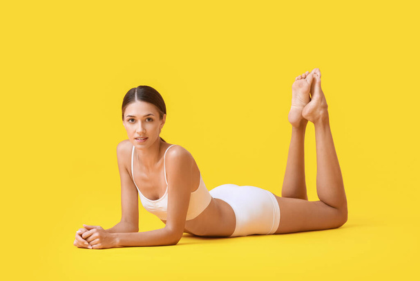 Young tanned woman in underwear lying on yellow background - Zdjęcie, obraz