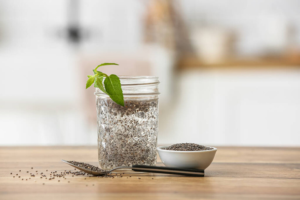 Bicchiere d'acqua, ciotola e cucchiaio con semi di chia in tavola in cucina - Foto, immagini