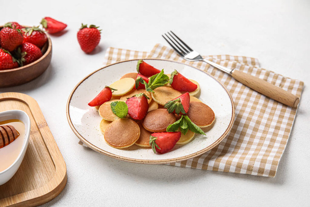 Plate with mini pancakes and delicious strawberry on light table - Foto, imagen