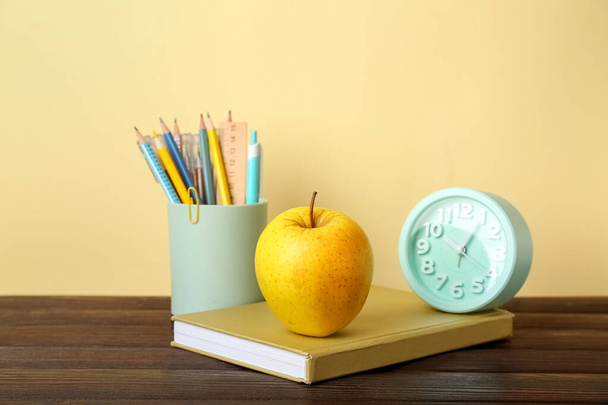 School stationery with apple and alarm clock on table against color background - Photo, Image