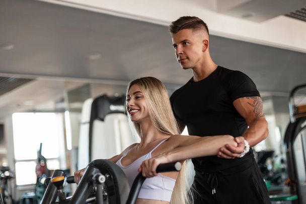 Happy beautiful smiling fitness woman and stern strong man athlete instructor train and workout together in the gym - 写真・画像