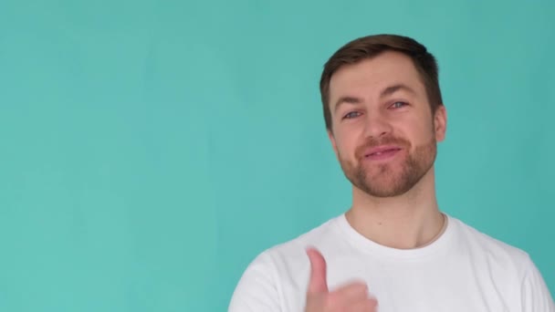 Handsome male guy pointing his thumb at empty space for copy, isolated background in studio. The guy recommends the case, pays your attention, the video is intended for advertising - Séquence, vidéo