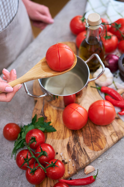 woman blanching a tomato holding over pan with hot water for further peeling. - Foto, Imagem