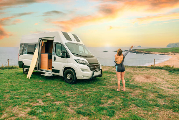 Unrecognizable young woman putting on her wetsuit for surfing next to her camper van - Foto, immagini