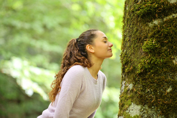 Profile of a happy woman smelling moss in a tree in a forest - Foto, afbeelding