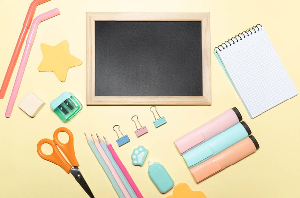 Background with school material, on yellow background. Blackboard for text. Accessories with pastel colours. - Foto, imagen