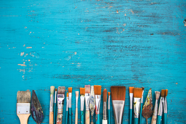 Artistic art supply utensils with paintbrushes on turquoise wooden background with copy space. Flat lay photo - Φωτογραφία, εικόνα