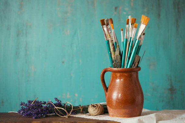 Still life of paint brushes  in clay jug an lavender flower on vintage turquoise background - Fotografie, Obrázek
