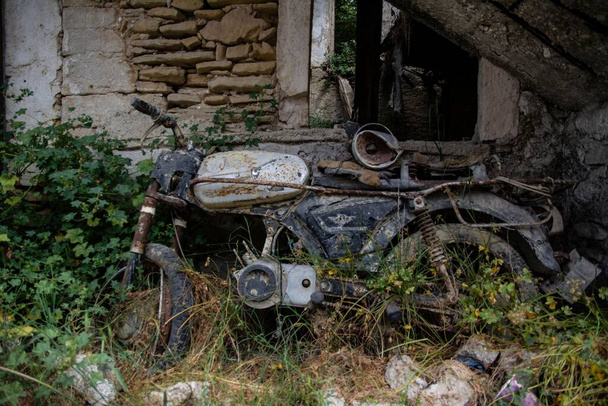 An old rusty bike parked in an abandoned garden against a damaged wall surrounded by plants - Foto, imagen