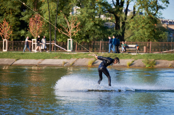 Wakeboarder faire des tours en se réveillant sur le lac. Jeune homme surfeur s'amusant wakesurf dans le parc du câble. Sport nautique, concept d'activité de plein air. - Photo, image