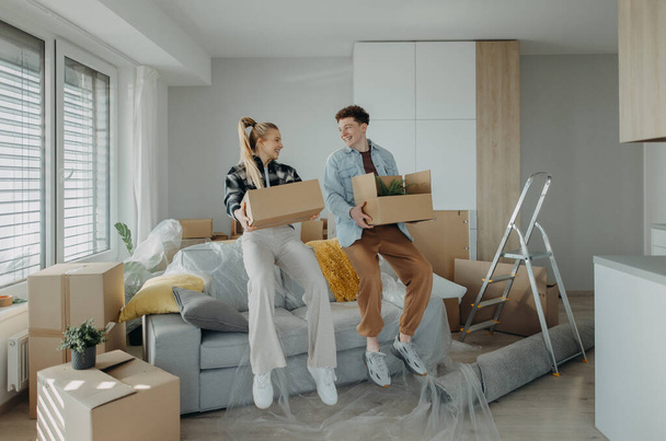 A cheerful young couple in their new apartment, carrying boxes. Conception of moving. - Foto, Bild