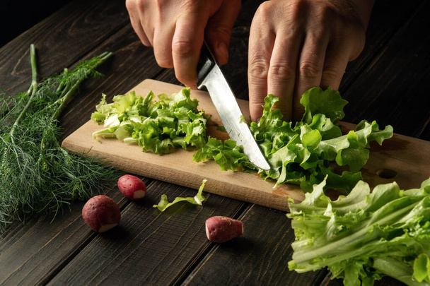 Bir aşçının eli, vejetaryen yemeği hazırlamak için bir bıçakla kesme tahtasının üzerinde yeşil yapraklar keser.. - Fotoğraf, Görsel