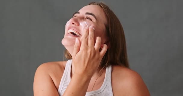 Young female laughing smiling and having fun while putting face cream on her face. High quality 4k footage - Filmagem, Vídeo