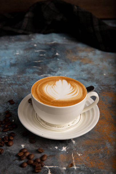 A vertical shot of a latte in a white coffee cup and coffee beans on a - Фото, зображення