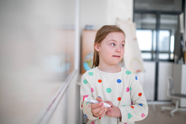 A little schoolgirl with down syndrome standing in front of whiteboard - Fotó, kép