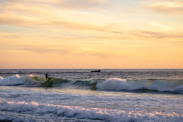 Ένας σέρφερ στα κύματα στη θάλασσα κατά τη διάρκεια του ηλιοβασιλέματος - Φωτογραφία, εικόνα