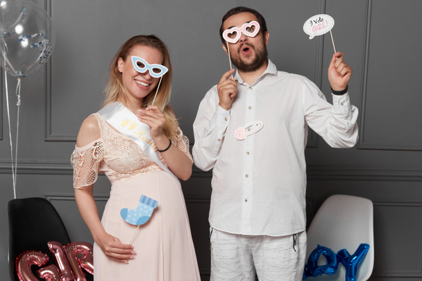 Front image of a smiling couple holding inscription boy or girl during gender reveals party, over props and balloons. - Foto, Imagen