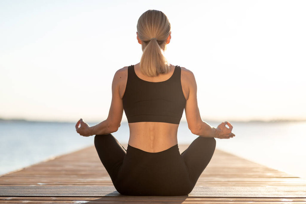 Wellness Concept. Rear View Of Sporty Woman Meditating Outdoors On Wooden Pier, Unrecognizable Slim Female Sitting In Lotus Position, Fit Lady Practicing Morning Yoga Near Lake Or Sea, Copy Space - Foto, afbeelding
