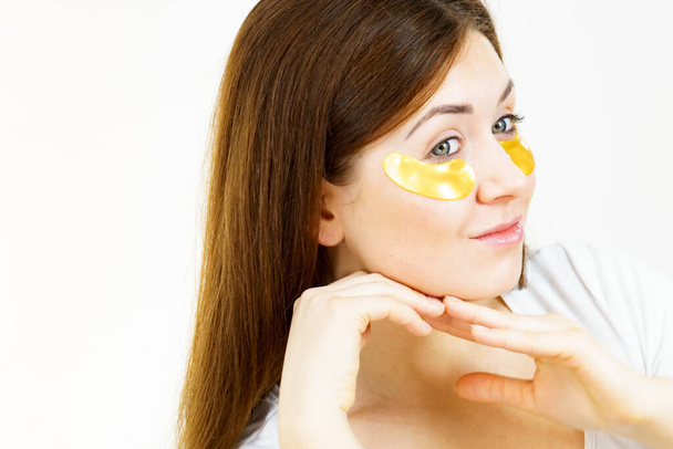 Young woman with golden collagen patches, under eye pads. Mask removing wrinkles and dark circles. Girl taking care of delicate skin around eyes. Beauty treatment. - Φωτογραφία, εικόνα