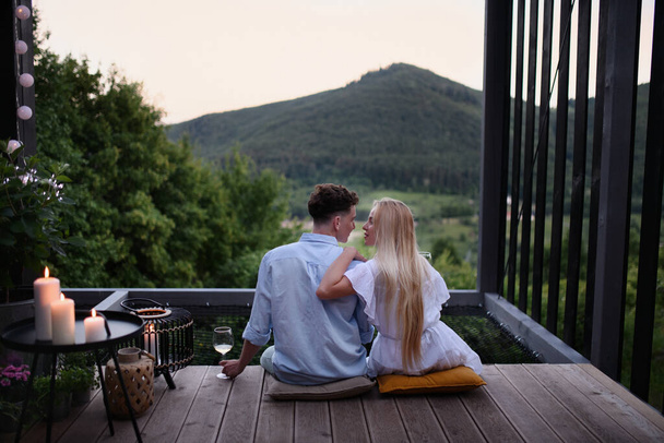 A young couple resting outdoors on terrace of tiny house in woods with view in evening, weekend away in tiny house in countryside, sustainable living. - Foto, immagini