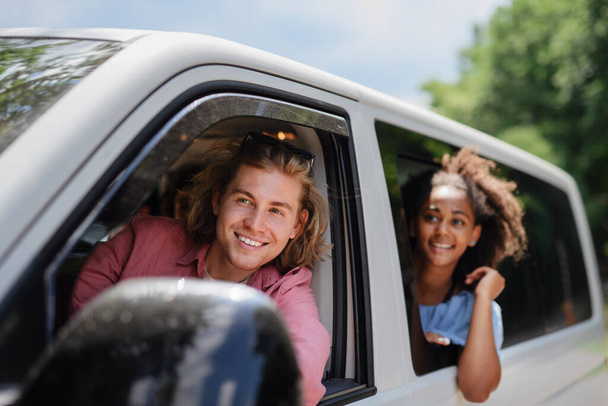 Multiracial young friends travelling together by car, looking through the window and smiling - summer vacation, holidays, travel, road trip and people concept. - Foto, afbeelding