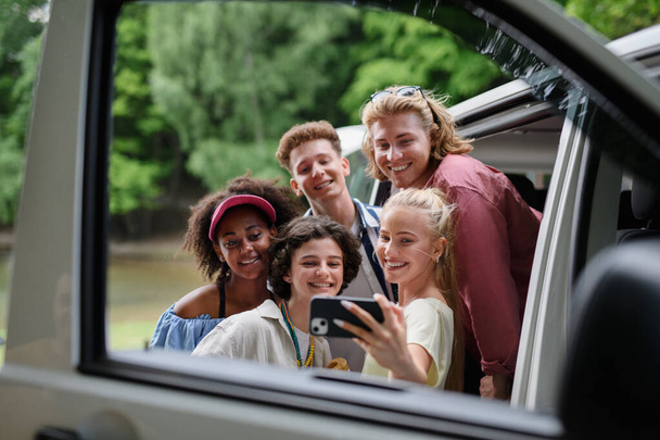 A multiracial young friends travelling together by car, taking selfie - summer vacation, holidays, travel, road trip and people concept. - Φωτογραφία, εικόνα