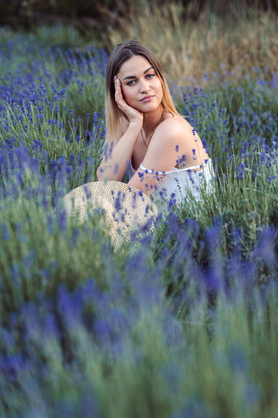 Vertical Photo Woman Sits among lavender, Looks thoughtfully into Camera. Girl without Retouching on Natural Background in lavender meadow outside city. - Zdjęcie, obraz