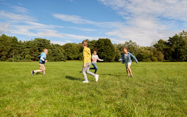 childhood, leisure and people concept - group of happy kids playing tag game and running at park - Photo, image