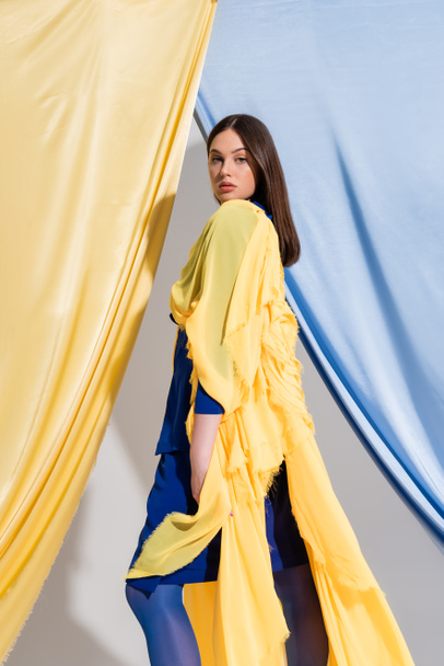 pretty young ukrainian woman in color block dress posing near blue and yellow curtains  - Valokuva, kuva