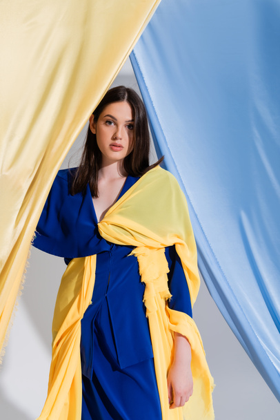 ukrainian woman in color block dress posing near blue and yellow curtains  - Foto, afbeelding