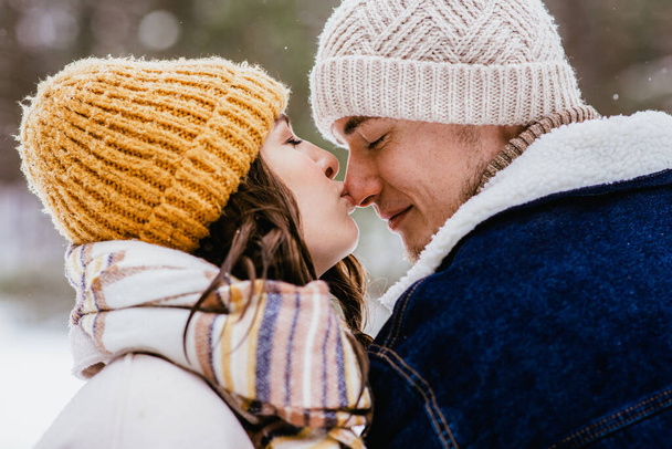 people, love and leisure concept - happy woman kissing mans nose in winter forest - Foto, imagen