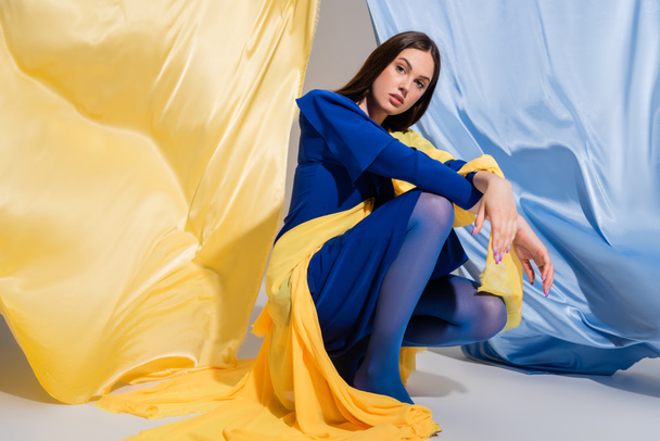 young ukrainian woman in stylish color block clothing sitting near blue and yellow fabric - Photo, Image