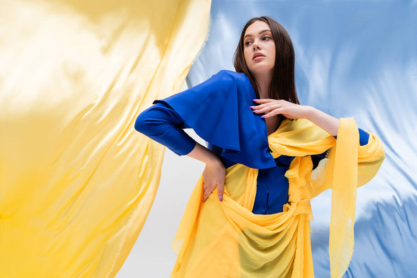 ukrainian young woman in fashionable color block clothing posing near blue and yellow fabric - Foto, imagen