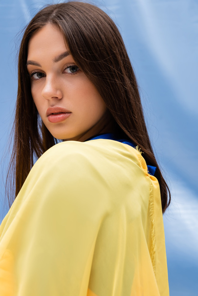 portrait of pretty ukrainian woman in yellow clothing looking at camera near blue fabric - 写真・画像