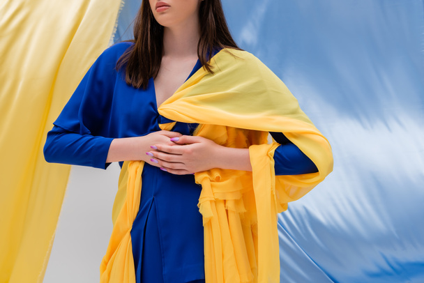 cropped view of patriotic ukrainian young woman in stylish clothing posing near blue and yellow fabric - Foto, afbeelding