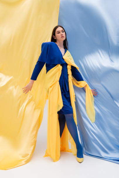 full length of patriotic ukrainian model in stylish outfit posing near blue and yellow fabric - Foto, Imagem